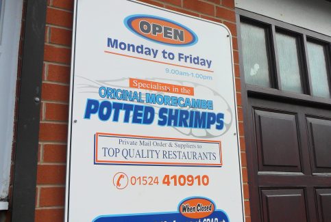 Photo of shop front sign at Baxter's fish shop giving details of opening hours and indicating that they are specialists in supplying Morecambe Bay potted shrimps.