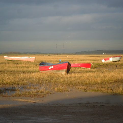 View from Sunderland Point showing four local fishing boats at low tide on grassy bank and electricity pylons in distance.