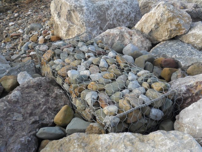 Close up image of a gabion, a wire cage filled with stones for defence against coastal erosion.